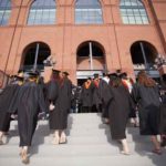 Students approach Michigan Stadium for commencement. Dressed in black robes, pictured from behind walking up stairs.