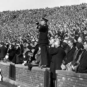 Nicholas Falcone conducting form atop the wall at Michigan Stadium