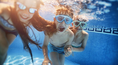 Brothers and sister are having fun playing tag underwater in the resort pool.