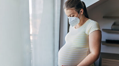 Pregnant mother wears mask indoors, stock photo