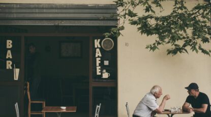 Two gentleman converse at an outdoor cafe.