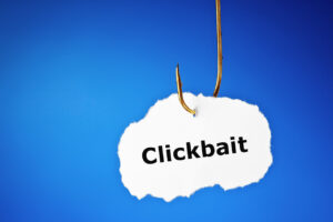 Printed word Clickbait hanging on a fishing hook. Concept about the misleading advertisements designed to attract attention and entice users to follow the linked piece of online content.