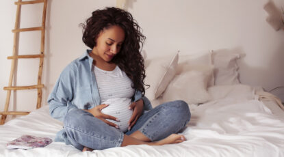 Young pretty african american woman pregnant laying in bed, lifestyle people concept close up