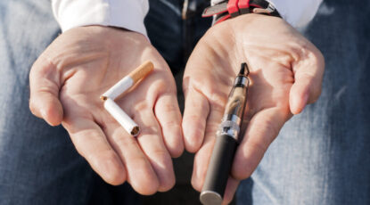 Two open palms display a broken cigarette and an e-cigarette.