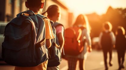 School children with backpacks walk toward school in golden hour.