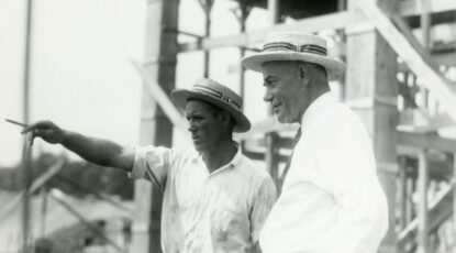 Fielding Yost observes construction of Michigan Stadium with foreman. Black and white. Two men wearing white straw skimmers.