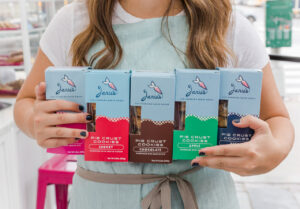 Woman holds five boxes of pie crust cookies produced by Janie's Life-Changing Baked Goods.