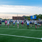 Michigan Marching Band practices under colorful sky.