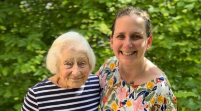 Two women, one who is elderly, stand together in front of greenery. The elderly woman was a pioneering female professor at U-M School of Public Health; the younger woman is a currently faculty member. Their families are connected because of the Holocaust.