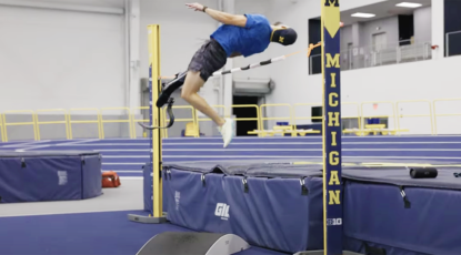 Paralympian with prosthetic leg executes a high jump in a Michigan atheltic setting.