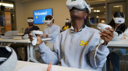 Student in Peter Toogood's "Augmenting Reality in Medicinal Chemistry" class wears virtual reality goggles with gray sweatshirt and block M at the University of Michigan's Center for Academic Innovation.