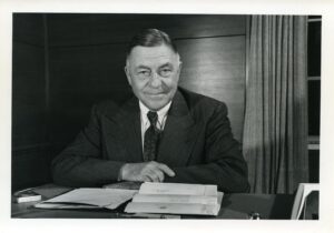 Alexander Ruthven seated at his desk. Black and white.