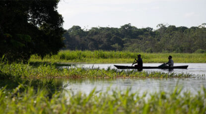 Two people row a canoe-like boat in the Amazon in Brazil.