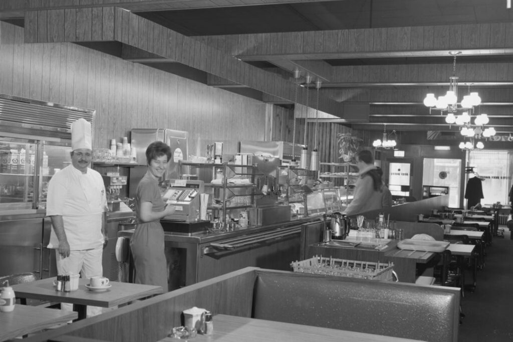 Black and white image of Curtis Restaurant interior with staff, 1968. Classic diner with cafeteria line and comfortable booths.