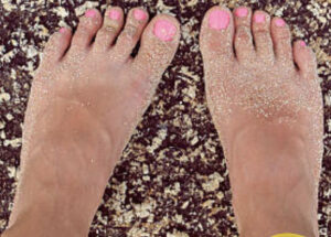 A pair of feet with pink toenails, covered in sand.