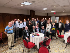 A group of people forms a semicircle around a table of seated people in a conference ballroom.