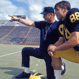 Color image of Wolverines football coach Bo Schembechler in 1969 kneeling at Michigan Stadium with team captain and tight end Jim Mandich.