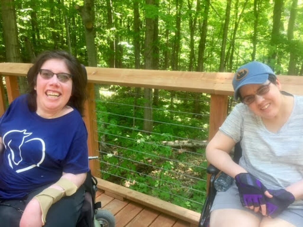 Two people with mobility challenges enjoy breathtaking views of Lake Michigan from a 300-foot-high platform, thanks to the Grand Traverse Regional Land Conservancy has created more than 3 miles of accessible trails since 2016 when the Overlook Trail at Arcadia Dunes opened.