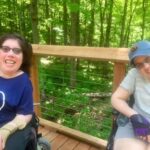 Two people with mobility challenges enjoy breathtaking views of Lake Michigan from a 300-foot-high platform, thanks to the Grand Traverse Regional Land Conservancy has created more than 3 miles of accessible trails since 2016 when the Overlook Trail at Arcadia Dunes opened.