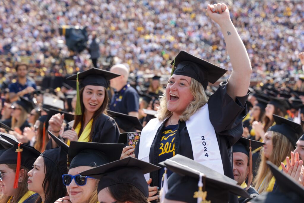 A female, first-generation college student, along with eight other students from Michigan's Upper Peninsula celebrate in caps and gowns during U-M Spring Commencement in Michigan Stadium.