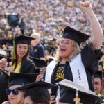 A female, first-generation college student, along with eight other students from Michigan's Upper Peninsula celebrate in caps and gowns during U-M Spring Commencement in Michigan Stadium.