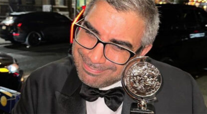 Tony winner Mike Mosallam, wearing glasses and with salt-and-pepper hair, cradles Tony award.