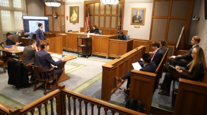 Typical courtroom scene with judge at front, jury box to the right and lawyers in the center, facing the judge.