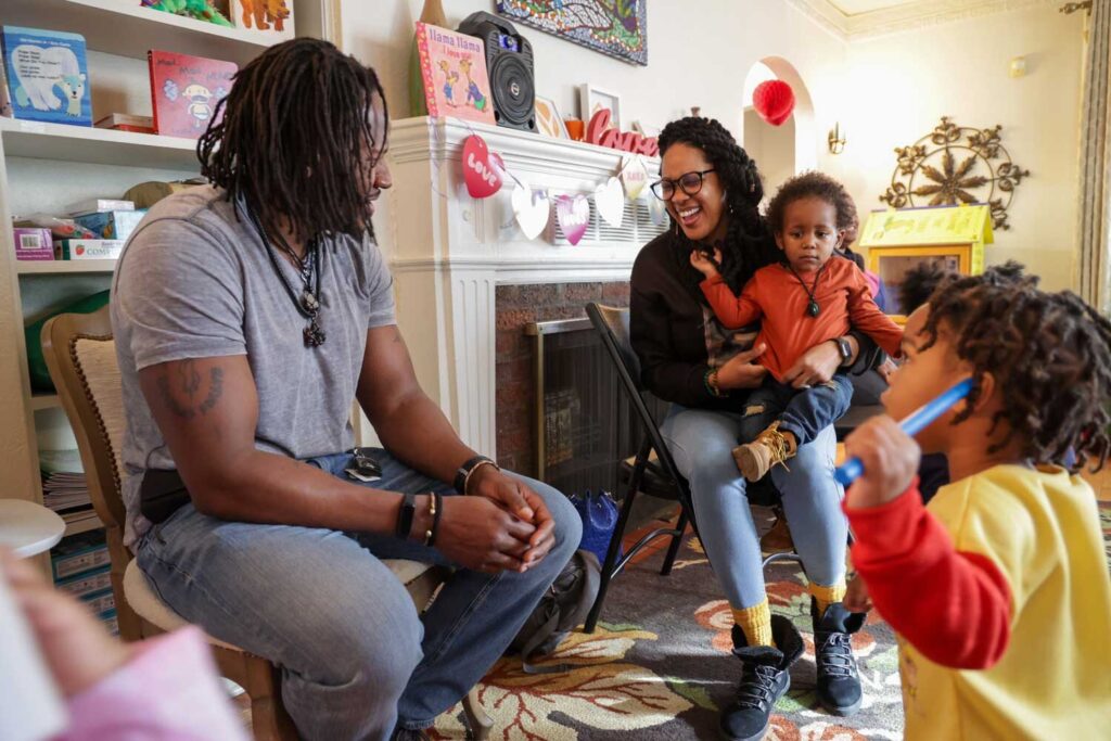 African American adults and children engage in play in a colorful educational setting in a living room in Detroit.