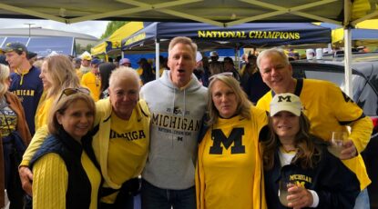 Michigan fans dressed in maize and blue tailgate before game.