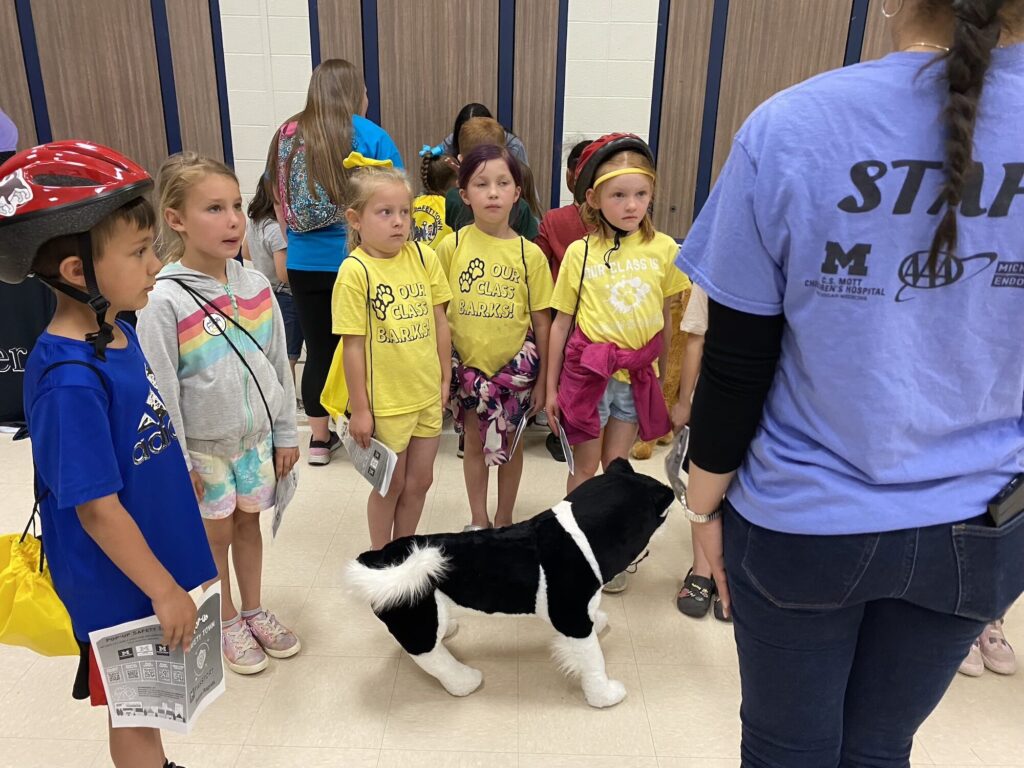 Children stand in a semicircle at the Pop-Up Safety town, modeled on the traditional Safety Town, a one-week injury prevention summer camp sponsored by school districts that uses permanent buildings and is expensive to develop. The the pop-up version makes it accessible to all.