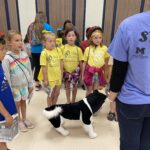 Children stand in a semicircle at the Pop-Up Safety town, modeled on the traditional Safety Town, a one-week injury prevention summer camp sponsored by school districts that uses permanent buildings and is expensive to develop. The the pop-up version makes it accessible to all.