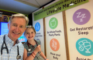 A smiling caucasian doctor and yung girl with stethoscope pose in front a poster touting Lifestyle Medicine.