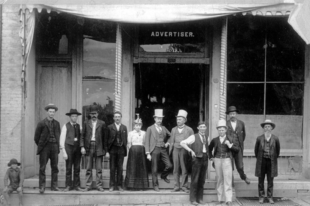 Black and white portrait of a group of men in the wild, wild west, standing on the steps of a building.