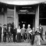 Black and white portrait of a group of men in the wild, wild west, standing on the steps of a building.