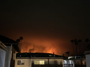 Small residential home with wildfire burning in the distance.