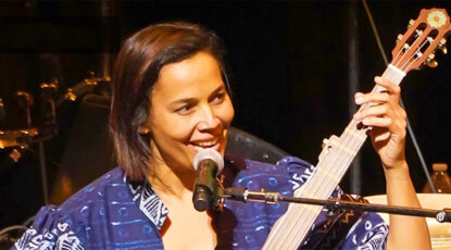 Beautiful woman, artist in residence at University of Michigan, plays bass guitar while seated at a microphone