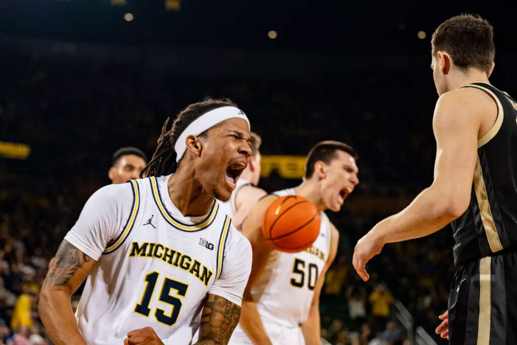 Michigan basketball player No. 15 Rubin Jones celebrates slamming home a missed layup against Purdue.