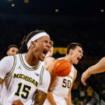 Michigan basketball player No. 15 Rubin Jones celebrates slamming home a missed layup against Purdue.