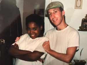 Filmmaker Davy Rothbart, a young caucasian man in cap and white t-shirt embraces a smiling African American girl.