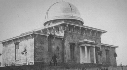 19th century b&w photo of a man in front of the domed Detroit Observatory at U-M in Ann Arbor. The man in the photograph is thought by some to be Henry Tappan himself, with one of his dogs, Leo or Buff.