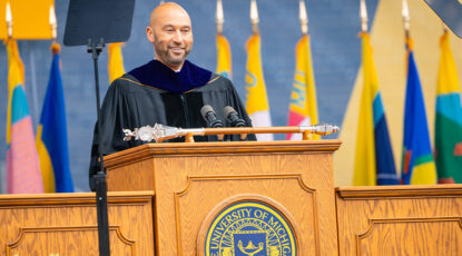 Derek Jeter speaks from the dais at Michigan Commencement dressed in all the graduation regailia.