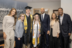 A group of people and graduates stand in a line smiling.