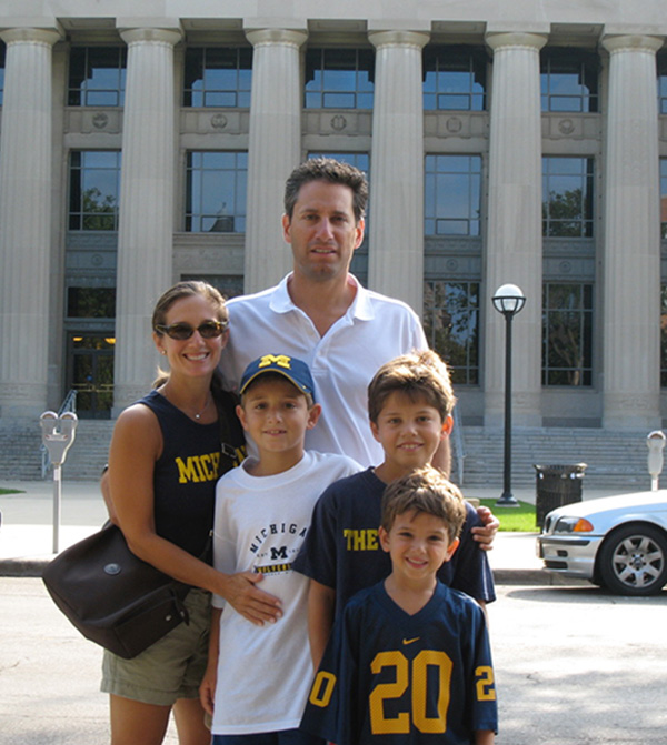 Two young parents and their three children, all dressed in University of Michigan gear, pose in front of Angell Hall.