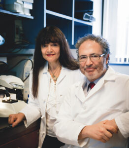 A female and male scientist, Castro and Lowenstein, working to cure pediatric cancer at Michigan Medicine. They are seated, wearing lab coats, surrounded by medical equipment.