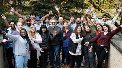 A team of happy researchers poses together outside on a sunny day.