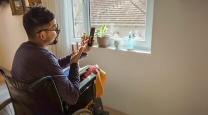 Bearded man in wheelchair uses cellphone to connect with telehealth provider.