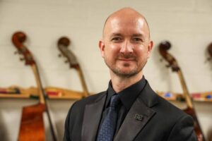 Jason Fettig said one of the most important things a musician can do is share their music through live performance. He is a bald and bearded caucasian man with instruments behind him.