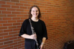 Maja Pechanach, who recently graduated from U-M with a Bachelor of Music in Performance, Winds & Percussion and majored in clarinet performance, said the tour experience was gratifying for her, as she loves music education. She is a young caucasian woman, holding her instrument, in front of a brick wall.