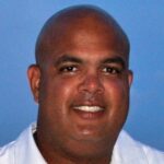 Headshot of bald man, nice smile. He is Warde Manuel, Michigan's Athletic Director.