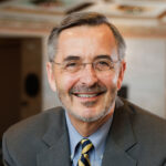 Headshot of U-M President Domenico Grasso. Salt-n-peppar hair, rimless spectacles, beard and friendly smile.